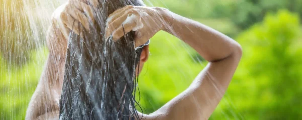 Une mère lave doucement les cheveux de sa fillette dans une salle de bain lumineuse, en massant le cuir chevelu du bout des doigts.
